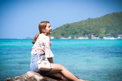 Young woman sitting on rock by sea