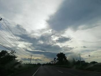 Road by electricity pylon against sky