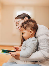 Mother reading book sitting with son at home