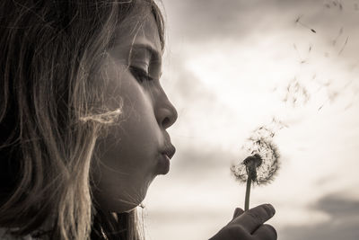 Close-up of young woman blowing dandelion