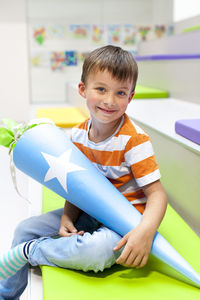 Portrait of boy holding cone while sitting on seat in classroom