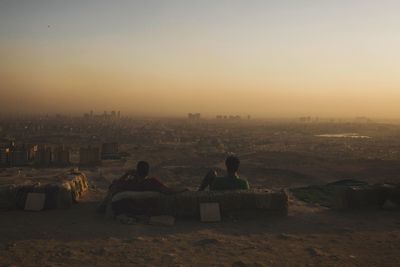 People sitting in city against clear sky during sunset