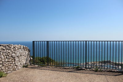 Railing by wall against clear blue sky