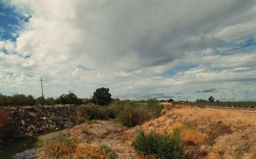 Dirt road in field against cloudy sky