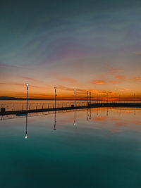 Reflection of bridge in water against sky during sunset