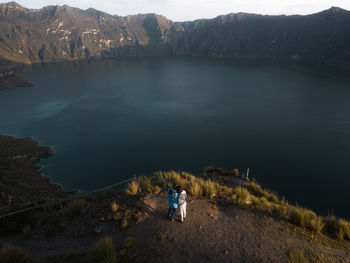 Couple standing in the mountains with lake behind drone view
