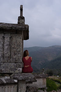 Rear view of woman sitting on mountain against sky