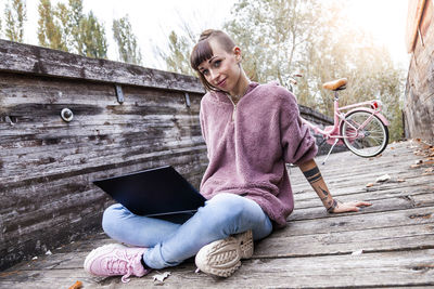 Young woman using mobile phone while sitting on wood