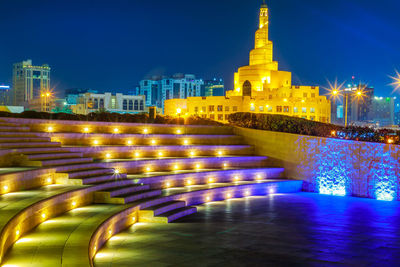 Illuminated buildings against blue sky at night