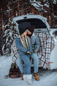 A loving young couple in an embrace sits in the trunk of a white car in winter 