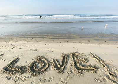 Love message written in sand on beach against sky