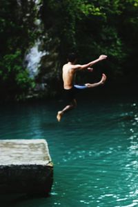 Rear view of shirtless man jumping in river