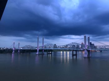 Suspension bridge over river against cloudy sky