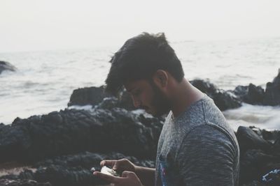 Side view of young man sitting on beach against clear sky