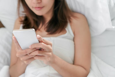 Midsection of woman using mobile phone on bed