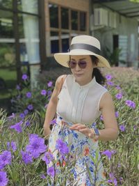 Young woman wearing sunglasses standing against purple flowering plants