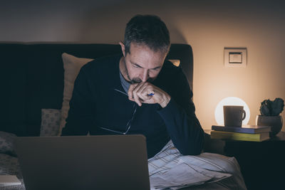 Man on bed after hard work with laptop until late at night. boy sitting in bedroom use online device