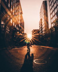 Man on city street by buildings against sky during sunset