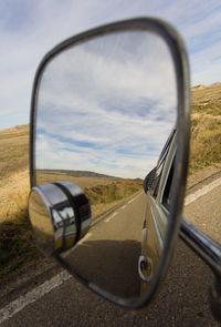 Close-up of side-view mirror against sky