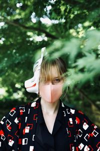 Portrait of young woman standing against tree