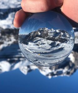 Close-up of hand holding crystal ball against snowcapped mountains