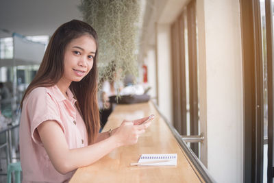 Side view of young woman using mobile phone in cafe