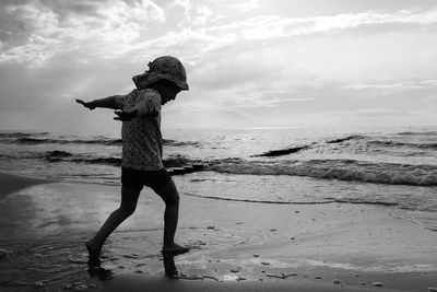 Girl with arms outstretched standing at beach against sky