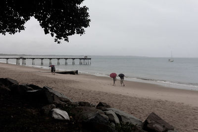 Two people wear umbrella are walking on the beach