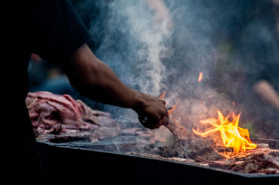 Midsection hand of man holding serving tongs by burning barbecue