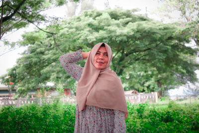 Portrait of smiling young woman standing against trees