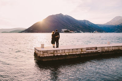 Rear view of couple standing on pier over lake against sky