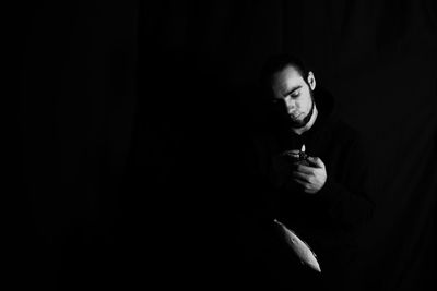 Portrait of young man smoking cigarette against black background