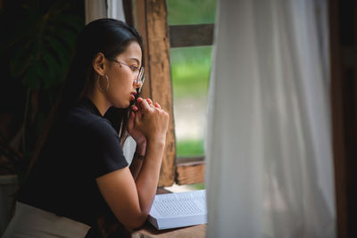 Young woman looking through window at home