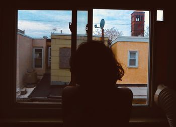 Rear view of woman looking through window at home