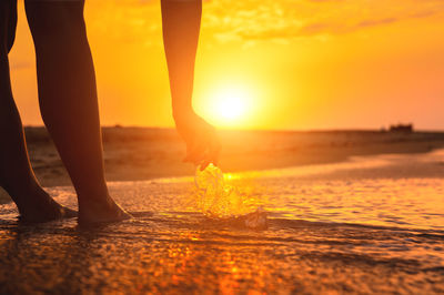 Low section of woman walking on beach during sunset