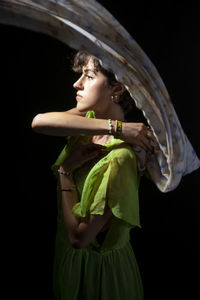 Portrait of young woman standing against black background