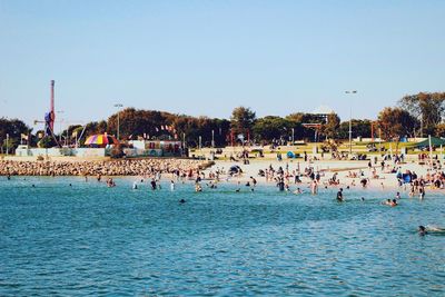 People swimming in sea against clear blue sky