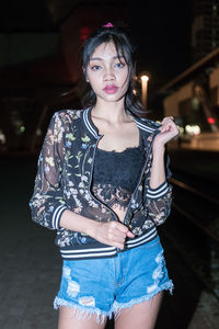 Portrait of beautiful young woman standing in city at night