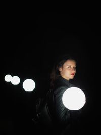 Portrait of young woman sitting against black background