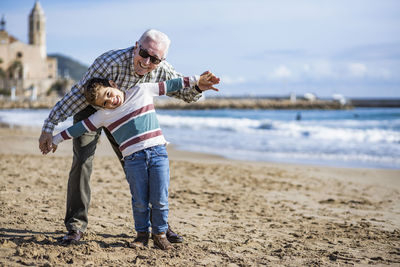 Portrait of happy senior man playing with grandson at beach