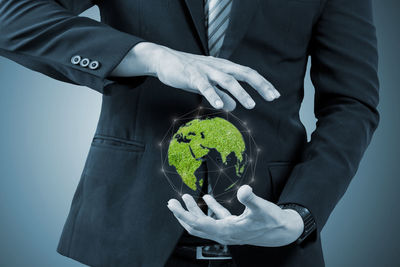 Digital composite midsection of businessman holding green globe