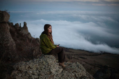 Rear view of woman sitting on rock against landscape