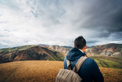 Rear view of hiker looking at mountains against cloudy sky