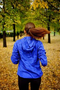 Rear view of woman running at leaves covered park during autumn