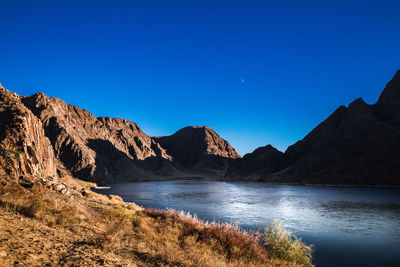 Scenic view of lake and mountains against clear blue sky