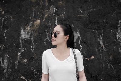 Young woman wearing sunglasses while standing against stone wall