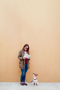 Woman with dog standing against wall