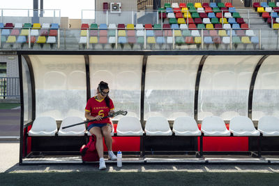 Player adjusting lacrosse stick at dugout