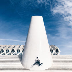 Low angle view of woman sitting on tower against cloudy sky