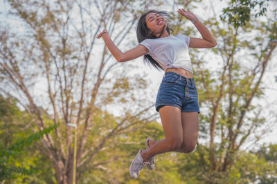 Low angle view of young woman jumping against trees